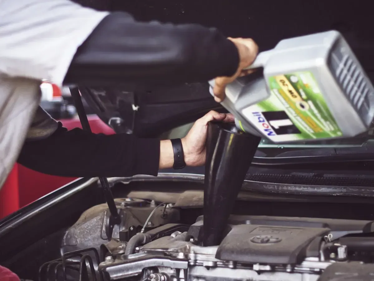 A mechanic topping up fluid in an engine bay